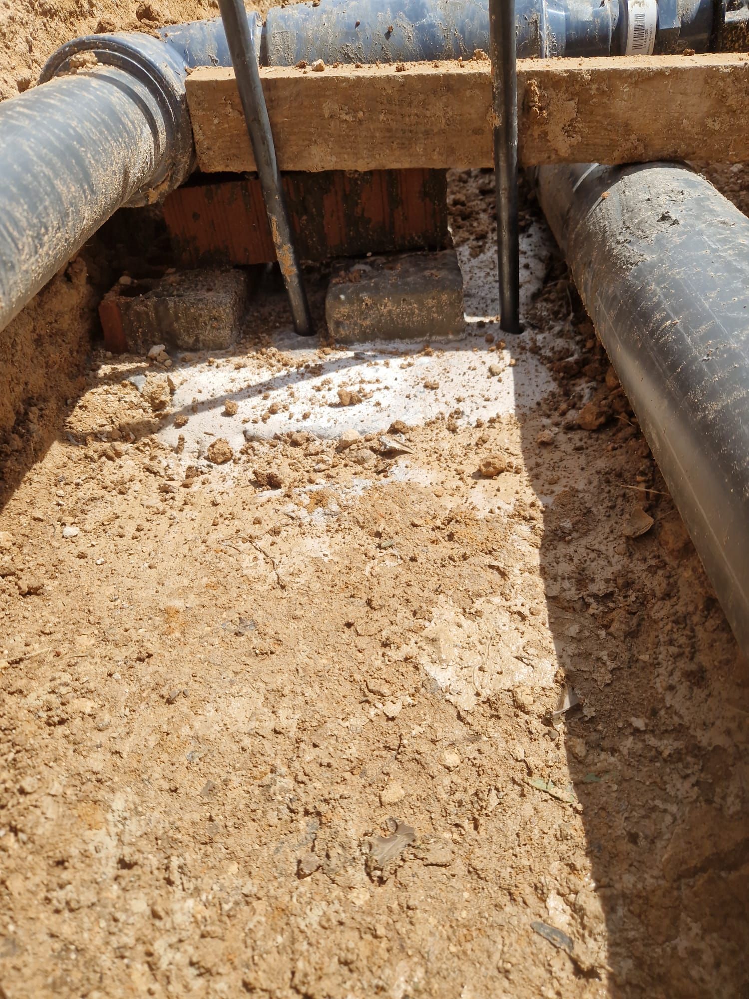 Zanja llena de barro con tuberías grandes y una losa de hormigón en una zona de excavación