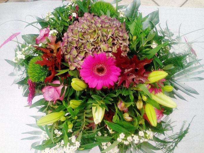 Farbenfroher Blumenstrauß mit einer leuchtend pinken Gerbera, grünem Laub und gemischten Blüten auf weißem Hintergrund