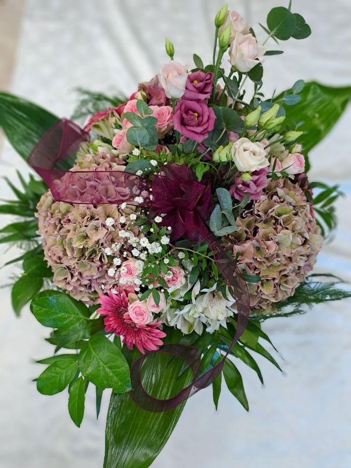 Rosa-bordeauxroter Blumenstrauß mit Grün und einem transparenten Band, in Zellophan verpackt