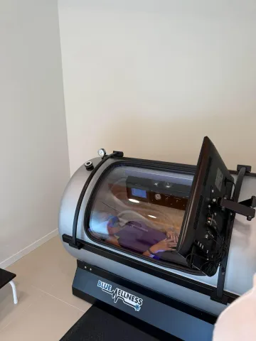 Persona dentro de una cámara hiperbárica. Máquina gris y negra en una habitación clara.