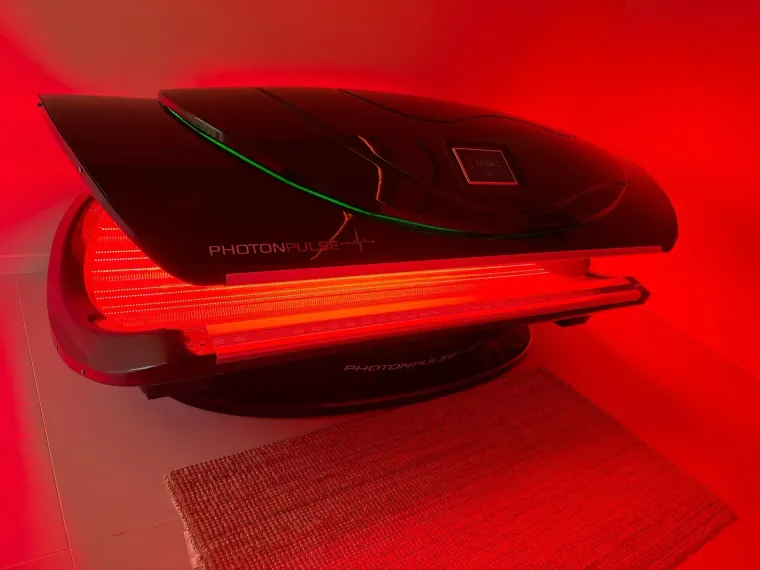 Dispositivo de terapia de luz roja con luz roja, vista en ángulo. Carcasa negra con línea verde.