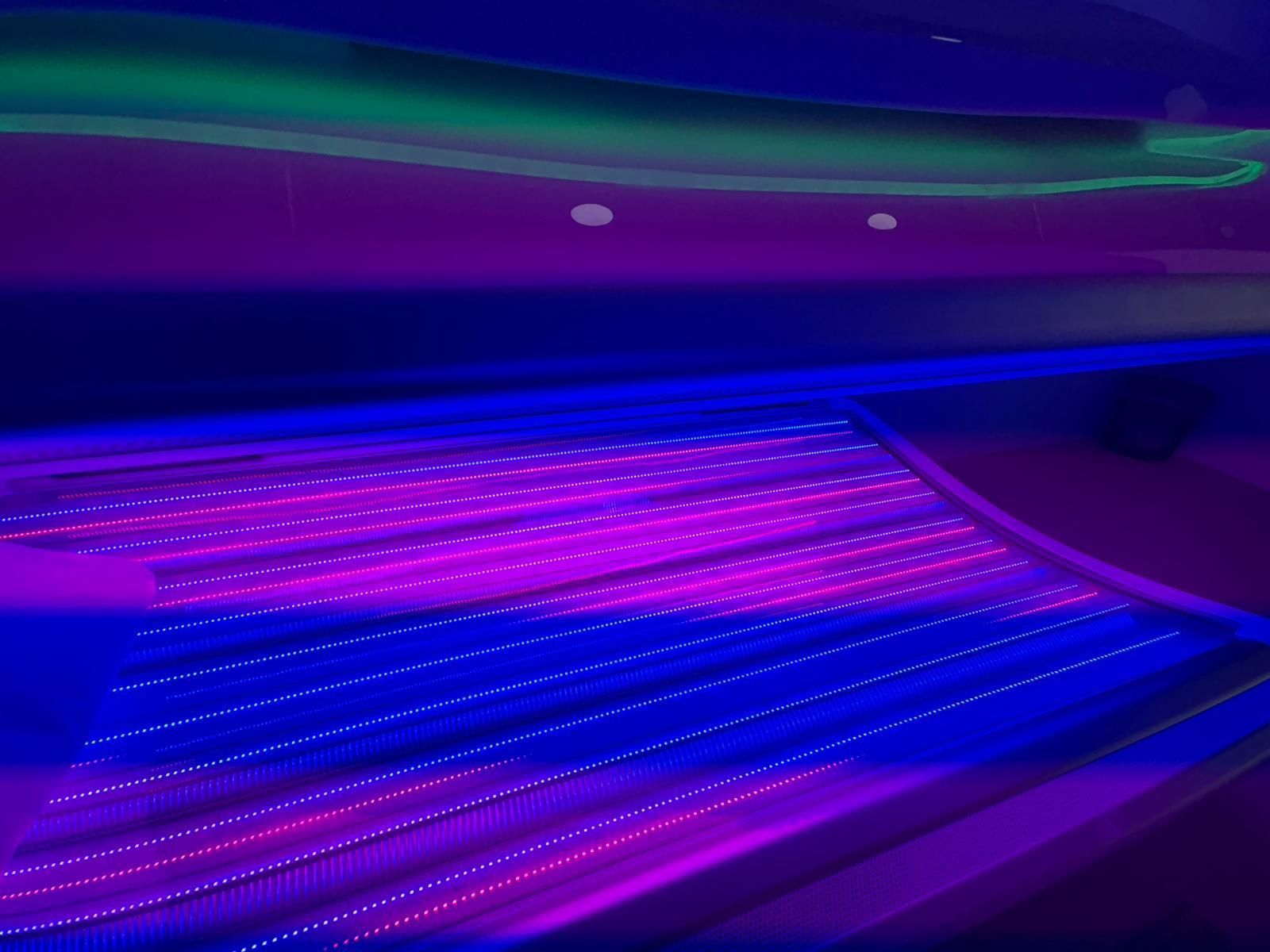 Interior brillante de color azul y morado, probablemente una cama de bronceado, con luces lineales y forma curva.