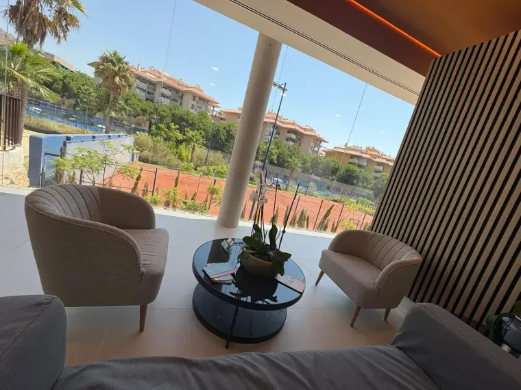 Moderna sala de estar con sillas de colores claros, mesa de centro negra, ventana grande y vista al exterior.