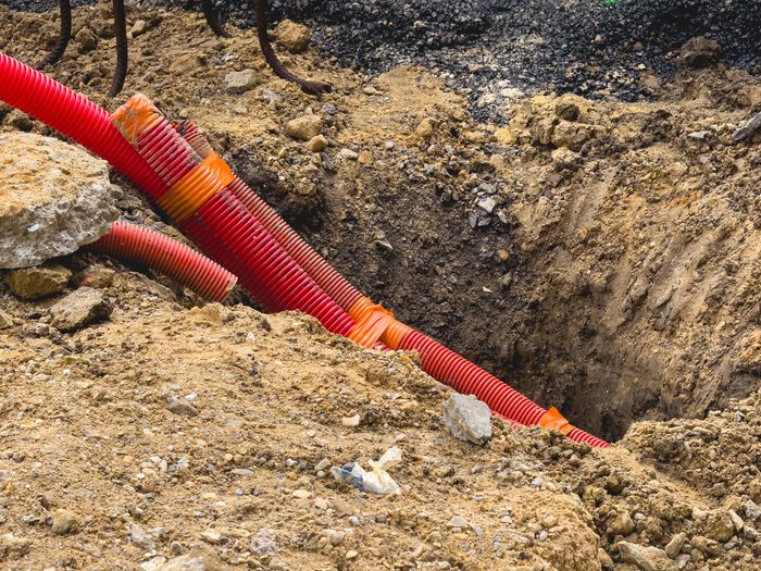Des tuyaux ondulés rouges sont posés dans une tranchée de terre sur un chantier de construction.