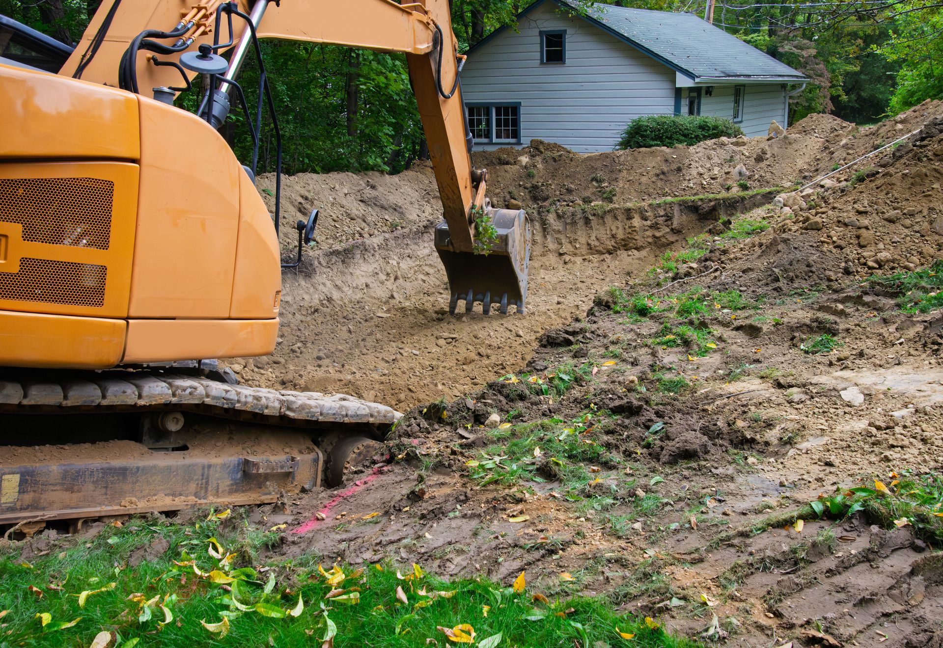 Une pelleteuse creuse un talus à côté d'une petite maison.