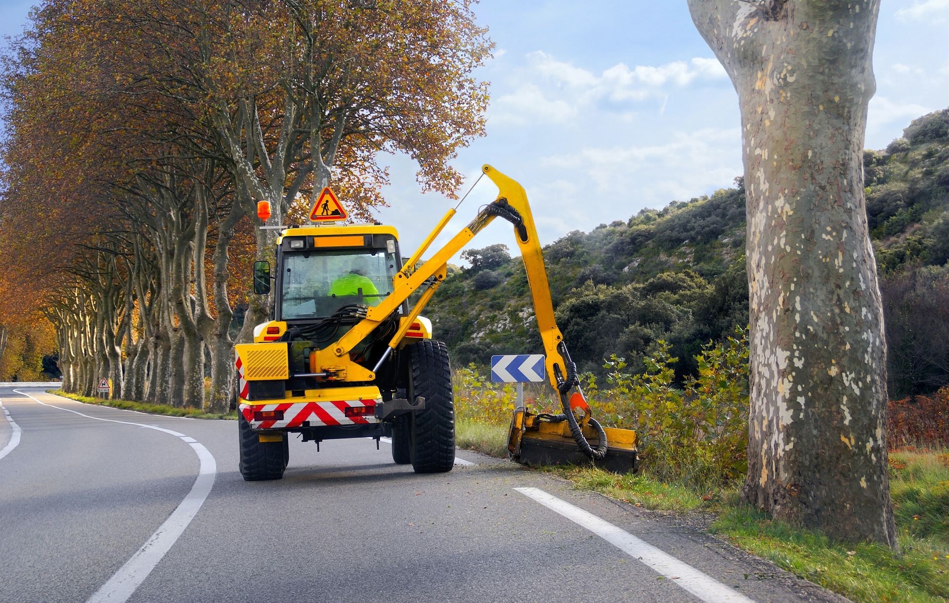 Un tracteur d'entretien routier coupe l'herbe au bord d'une route.