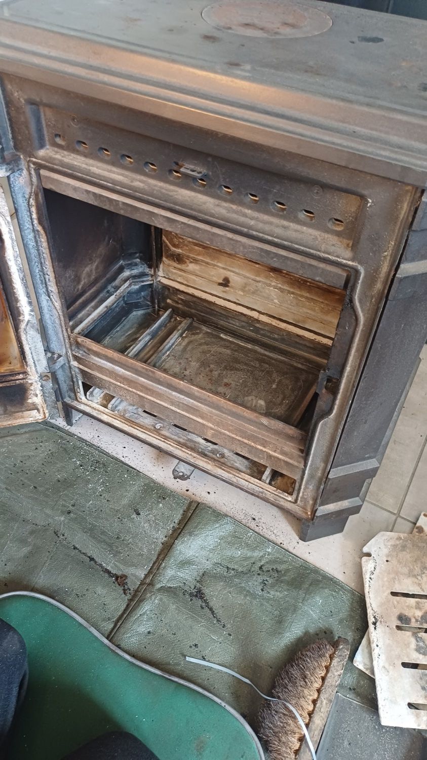 Poêle en métal rouillé ouvert, porte ouverte, dans un atelier ou un garage, laissant apparaître un foyer vide.