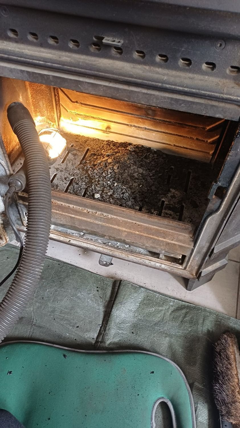 Poêle à bois ouvert avec un feu crépitant à l'intérieur et une chaise verte devant.