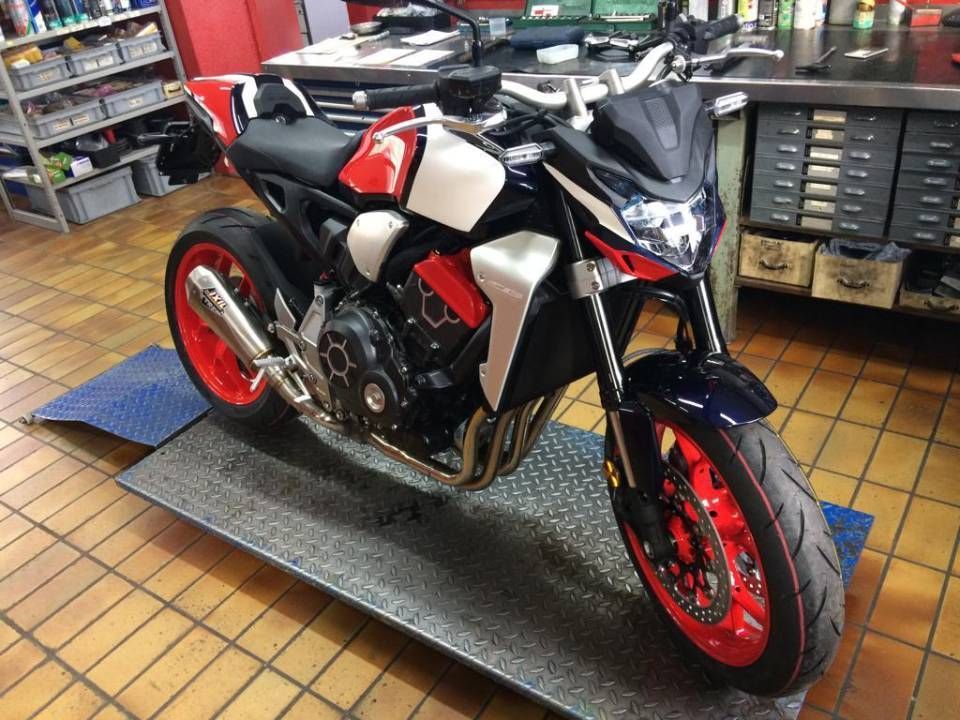 Ein rot-weiss-schwarzes Honda-Motorrad mit roten Felgen und Details steht auf einer Hebebühne in einer Werkstatt.