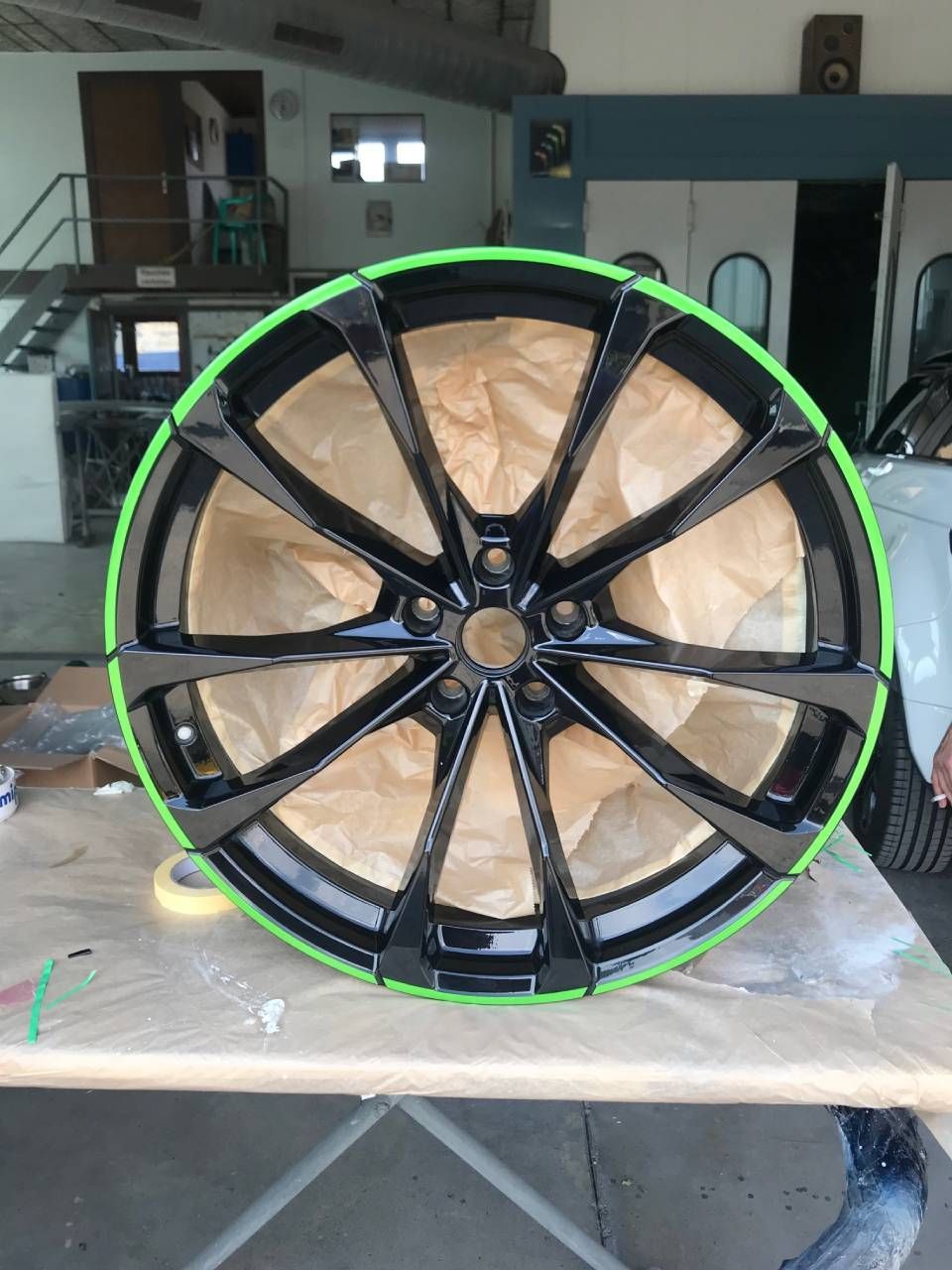 Schwarzes Autorad mit grünem Felgenrand, abgeklebt zum Lackieren, auf einem Tisch in einer Werkstatt.