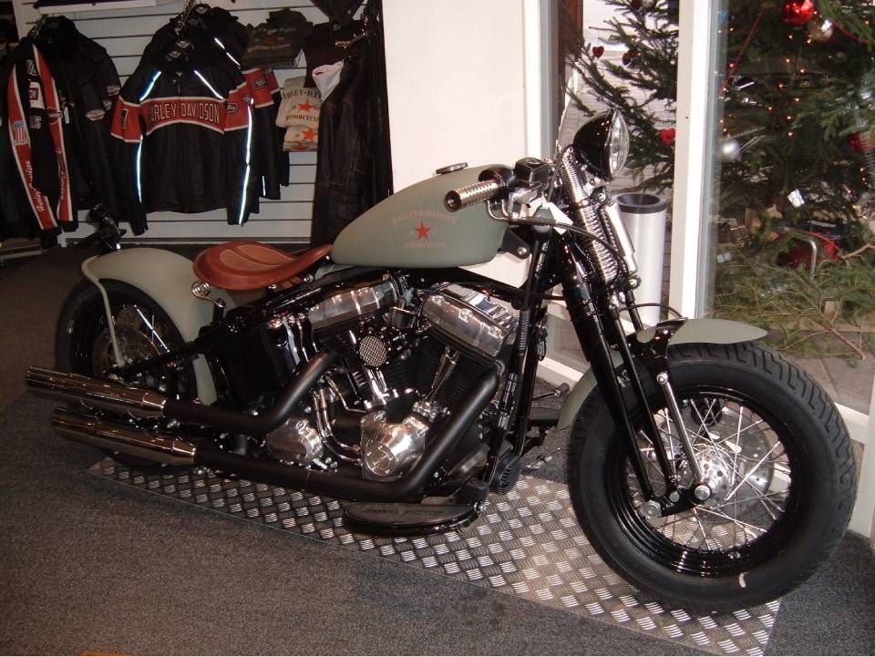 Olivgrünes Motorrad mit braunem Sitz, schwarzem Rahmen und Chromdetails, in einer Halle geparkt.