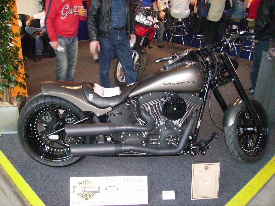 Bei einer Veranstaltung wird ein individuell gestaltetes graues Harley-Davidson-Motorrad mit schwarzen Akzenten und niedrigem Profil ausgestellt.