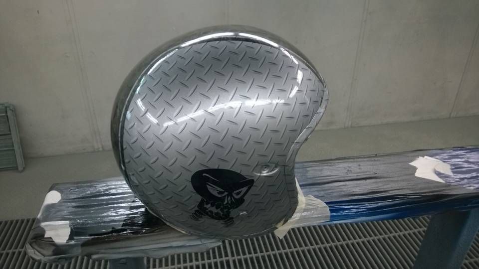 Silberner Motorradhelm mit Riffelblechmuster und Totenkopfmotiv.