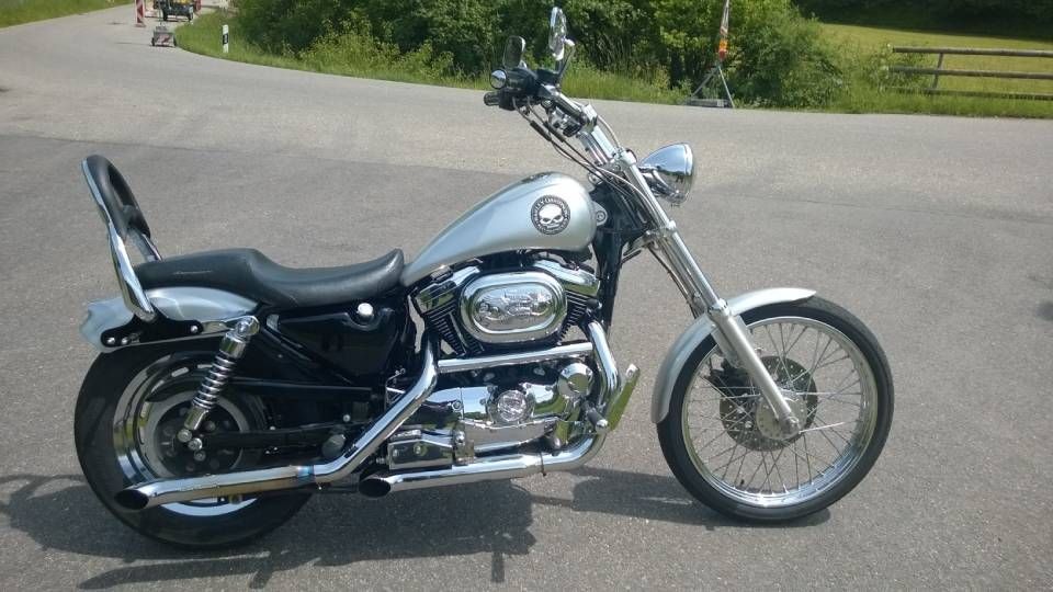 Eine silberne Harley-Davidson mit schwarzem Sitz und verchromtem Auspuff steht auf Asphalt.