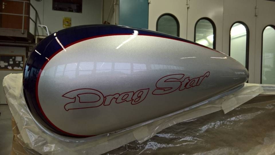 Silberner und blauer Motorradtank mit der Aufschrift „Drag Star“ in roter Schrift, in einer Werkstatt.