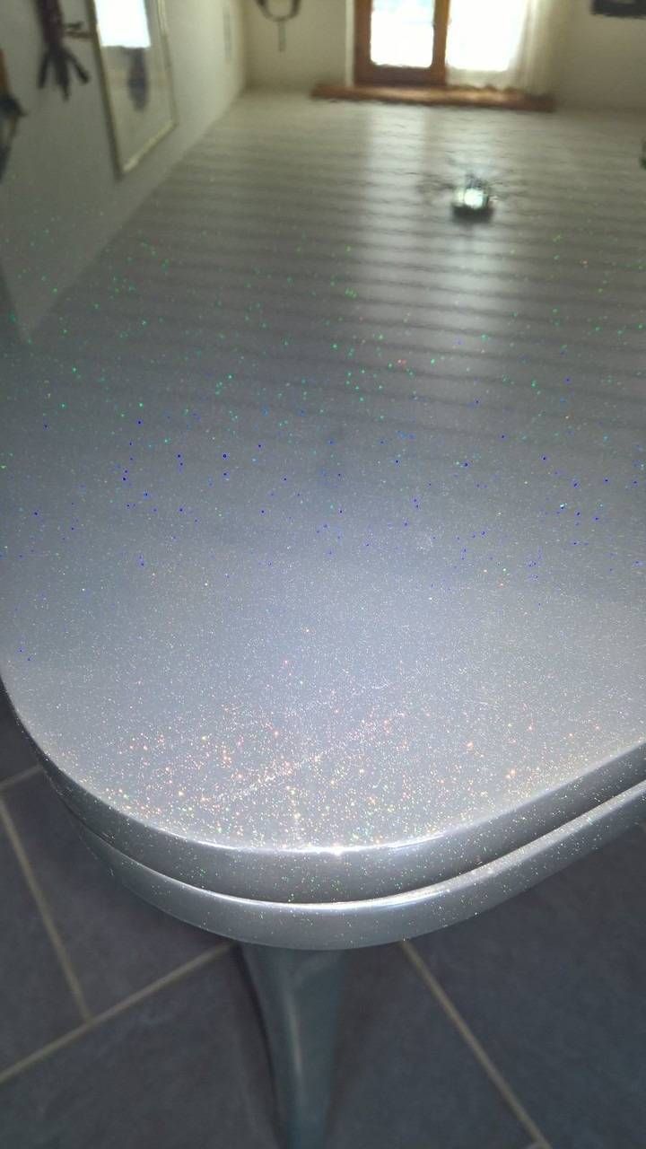 Nahaufnahme einer silbernen, glitzernden Arbeitsplatte mit abgerundeten Kanten, die den Raum reflektiert.