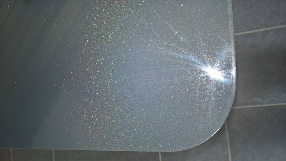 Abgerundete Ecke einer strukturierten, hellen Oberfläche, von der helles Licht reflektiert wird; dunkelgrauer Fliesenboden.