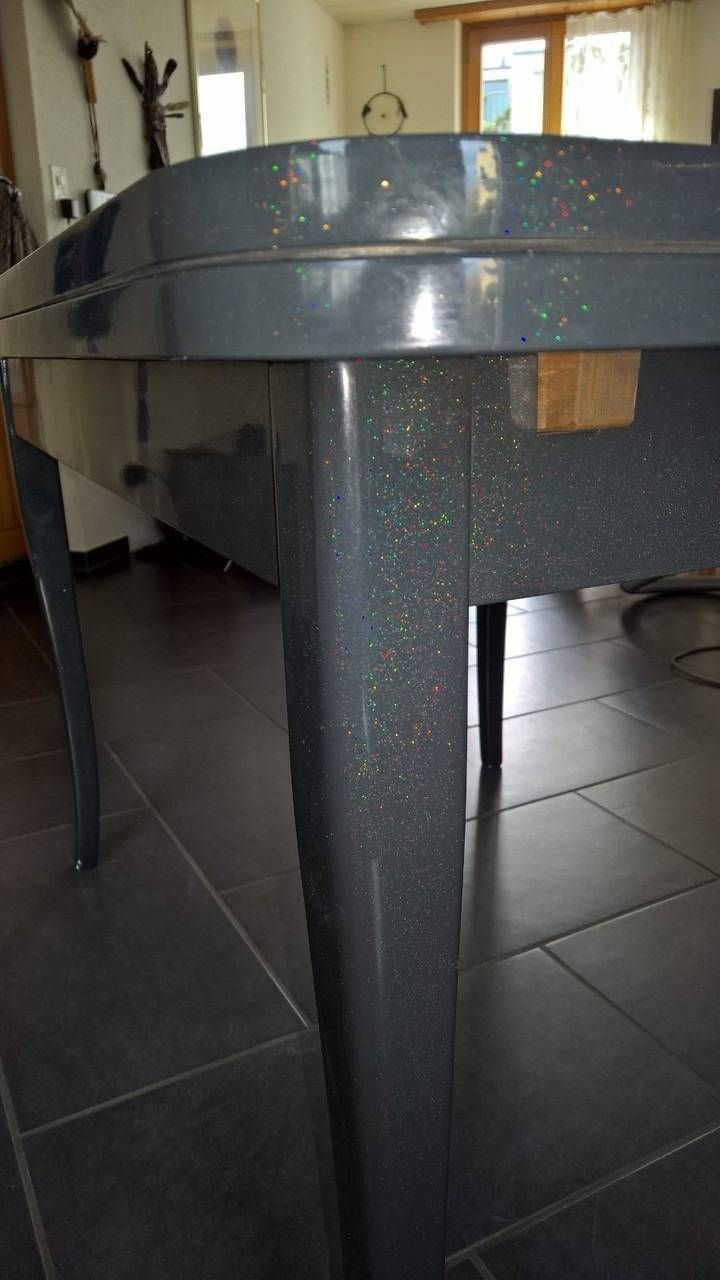 Grauer Tisch mit gesprenkelter Oberfläche und Beinen sowie einem dunklen Fliesenboden.