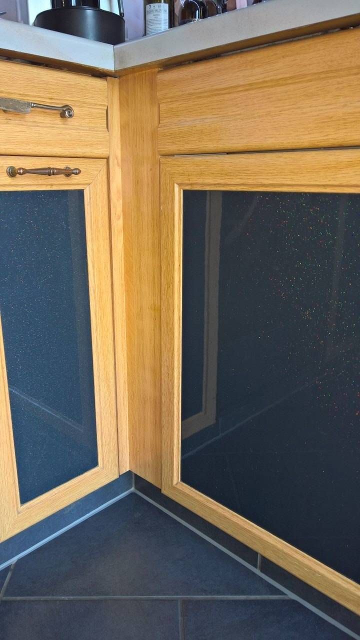 Küchenschränke aus Holz mit dunklen Glaspaneelen, Granitarbeitsplatte und dunklem Fliesenboden.