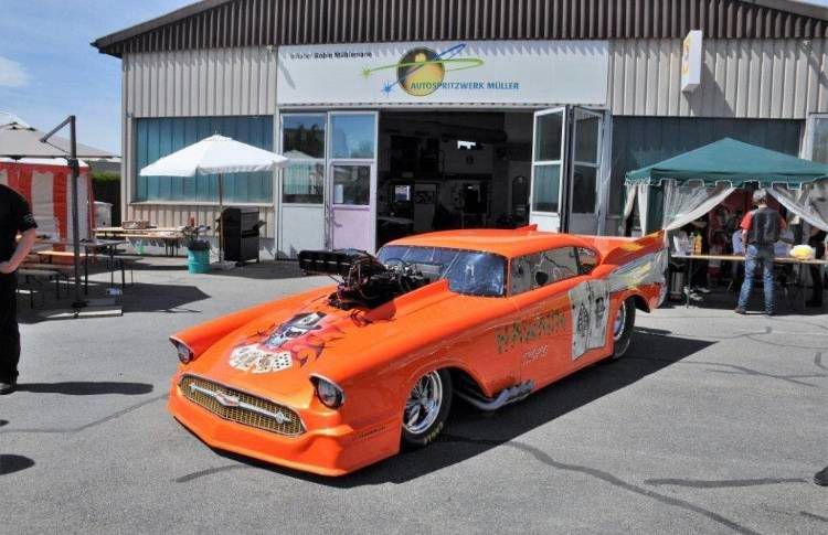 Ein orangefarbener Dragster parkt vor einem Gebäude mit offenen Türen.