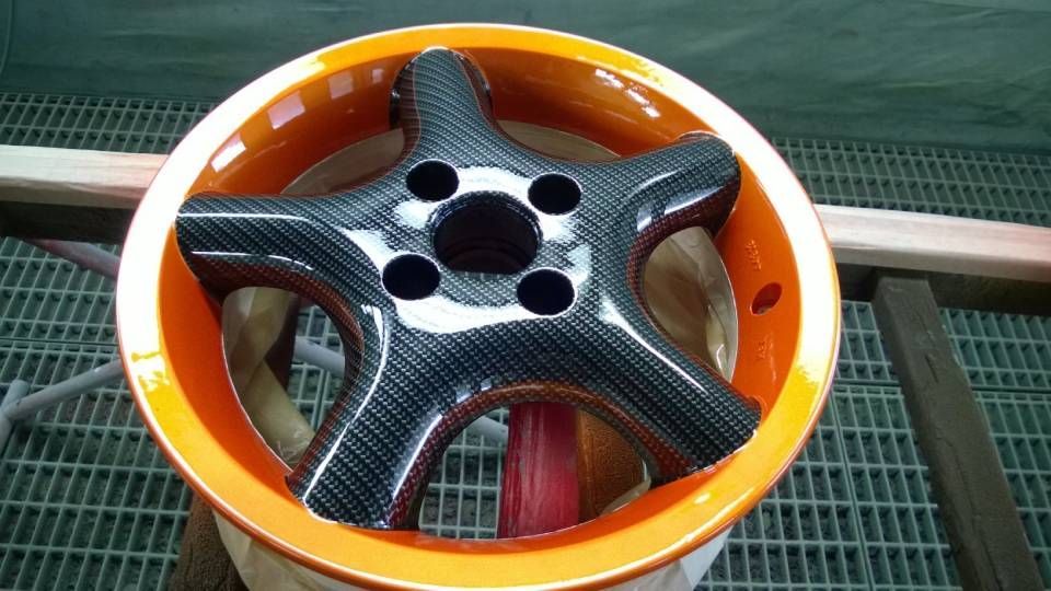 Carbonfaserrad mit orangefarbenem Felgenrand in einer Lackierkabine.