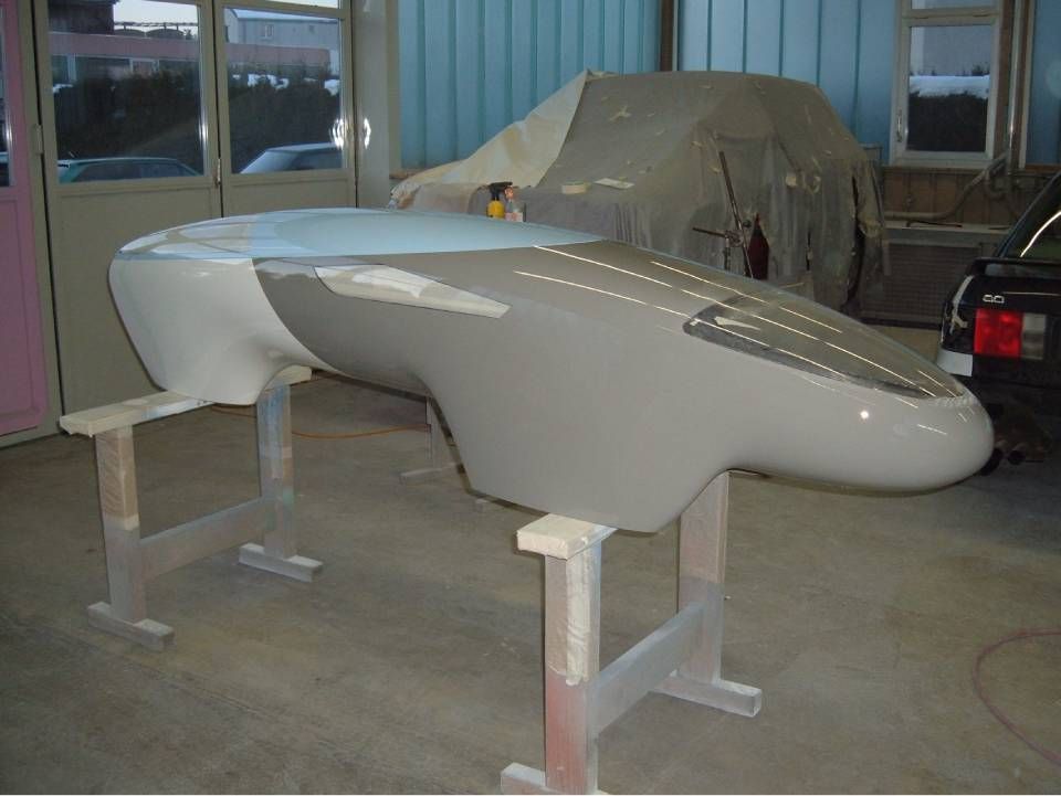 In einer Werkstatt ruht eine grau und weiss lackierte Fahrzeugkarosserie auf zwei hölzernen Sägeböcken.