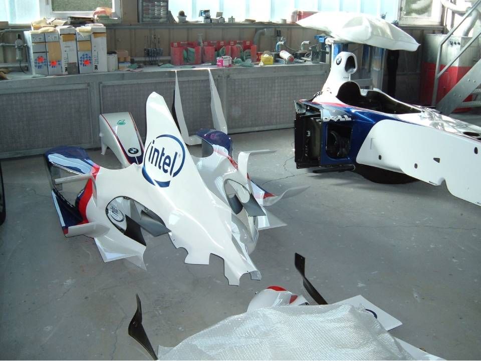 Weisse und blaue Formel-1-Autoteile mit der Aufschrift „Intel“ in einer Werkstatt. Im Hintergrund ist ein weiteres Auto teilweise montiert.