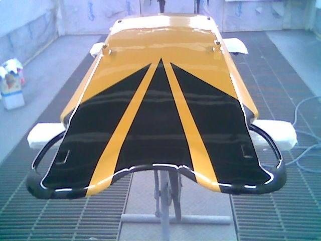 Ein gelb und schwarz bemalter Gegenstand, möglicherweise ein Schlitten, auf einem Ständer in einer Lackierkabine.