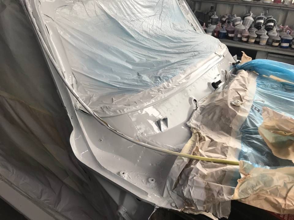 Mit Plastikfolie und Klebeband abgedeckte Karosserieteile sind in einer Werkstatt bereit zum Lackieren.