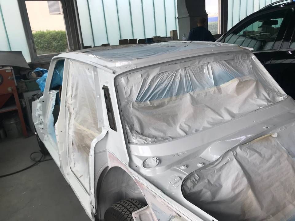 Das Auto wird in einer Werkstatt lackiert und ist mit Plastikfolie abgedeckt. Die Karosserie ist weiss und bereit zum Lackieren.