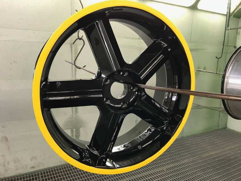 Schwarzes Autorad mit gelbem Felgenrand, das in einer Lackierkabine hängt.