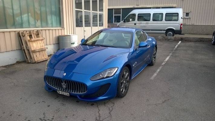 Ein blauer Maserati GranTurismo parkte in der Nähe eines Gebäudes und eines Lieferwagens.