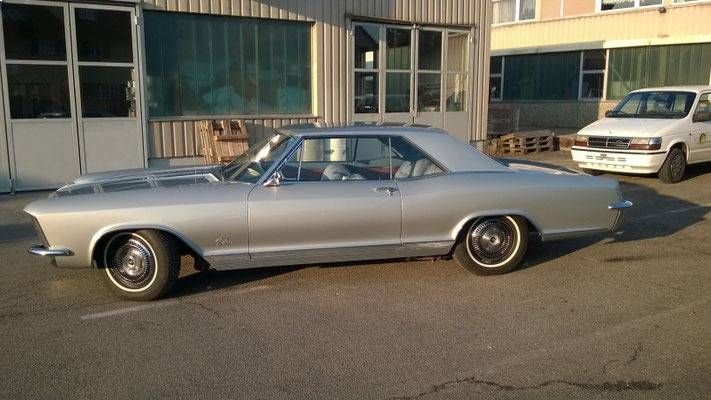 Ein silberner Buick Riviera Oldtimer parkt vor einem Gebäude.