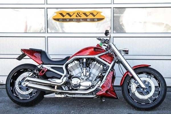 Ein rotes und verchromtes Harley-Davidson-Motorrad parkt vor einem weissen Garagentor mit dem Logo „W&W CYCLES“.
