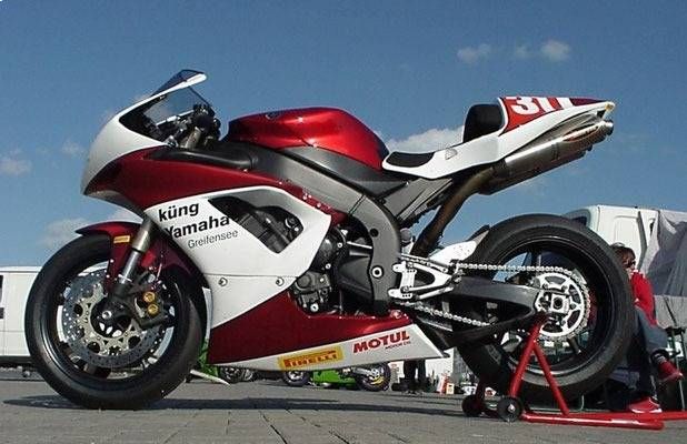 Ein rot-weiss-schwarzes Yamaha-Motorrad mit Rennlackierung steht im Freien auf einem Ständer.