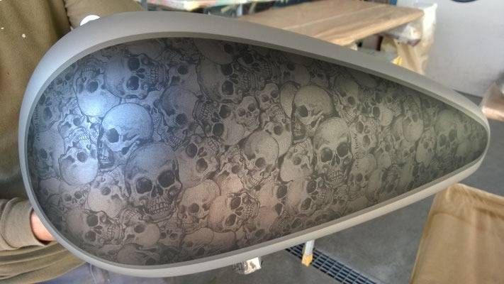 Motorrad-Benzintank mit Totenkopfmuster auf mattgrauer Oberfläche.
