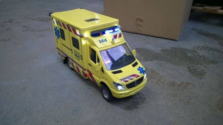 Gelber Spielzeugkrankenwagen mit blinkenden Lichtern auf grauem Untergrund.