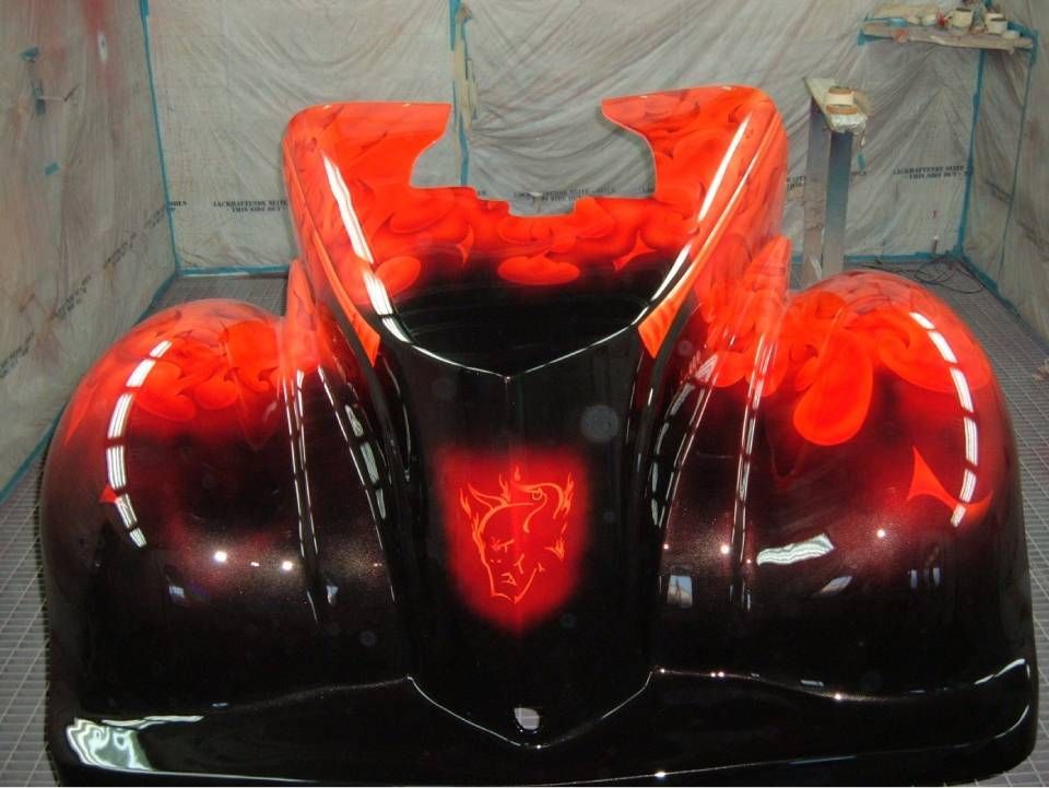 Schwarzer Kotflügel mit roten Flammen und rotem Emblem in einer Lackierkabine.