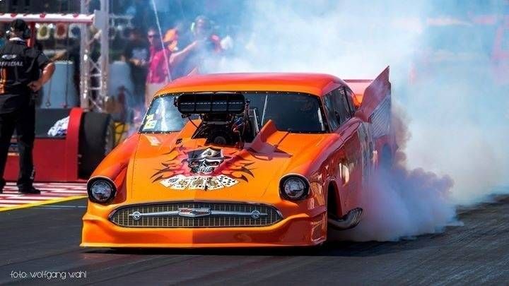 Oranger Dragster, dichte Rauchwolken, auf der Rennstrecke. Totenkopfmotiv auf der Motorhaube.