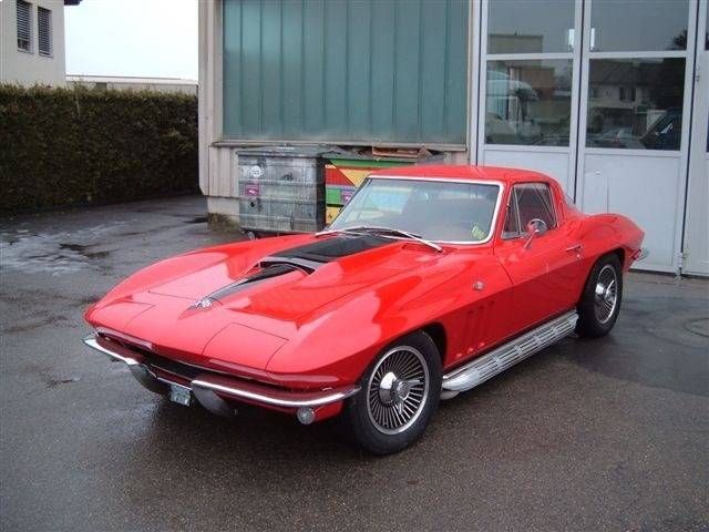 Ein rotes Corvette-Coupé aus den 1960er Jahren mit schwarzer Lufthutze steht vor einem Gebäude.