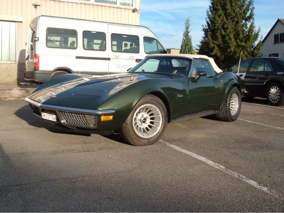 Ein grünes Corvette-Cabriolet steht auf einem Parkplatz, im Hintergrund sind ein weisser Lieferwagen und weitere Autos zu sehen.