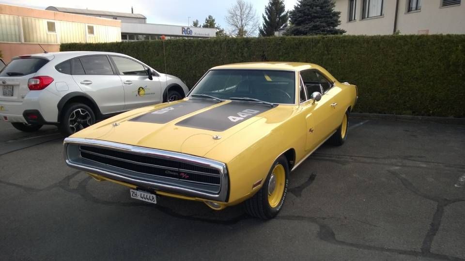 Ein gelber Oldtimer-Dodge Charger mit schwarzen Rennstreifen parkt neben einem weissen SUV.