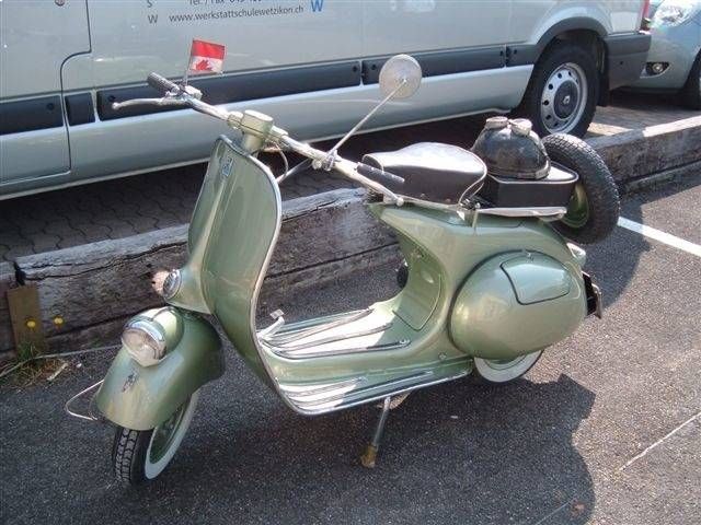 Ein grüner Vintage-Vespa-Roller parkt neben einem hellgrünen Lieferwagen, hinten ist ein Reserverad montiert.