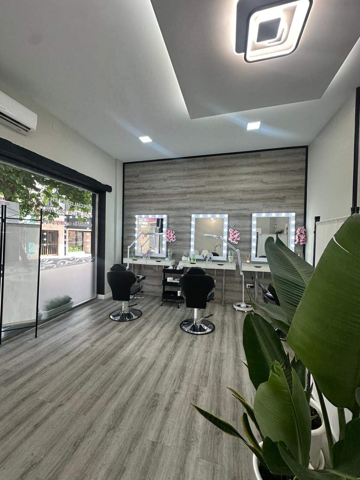 Interior de peluquería con tres puestos de peluquería, espejos y sillas negras. Suelo y pared de madera clara.