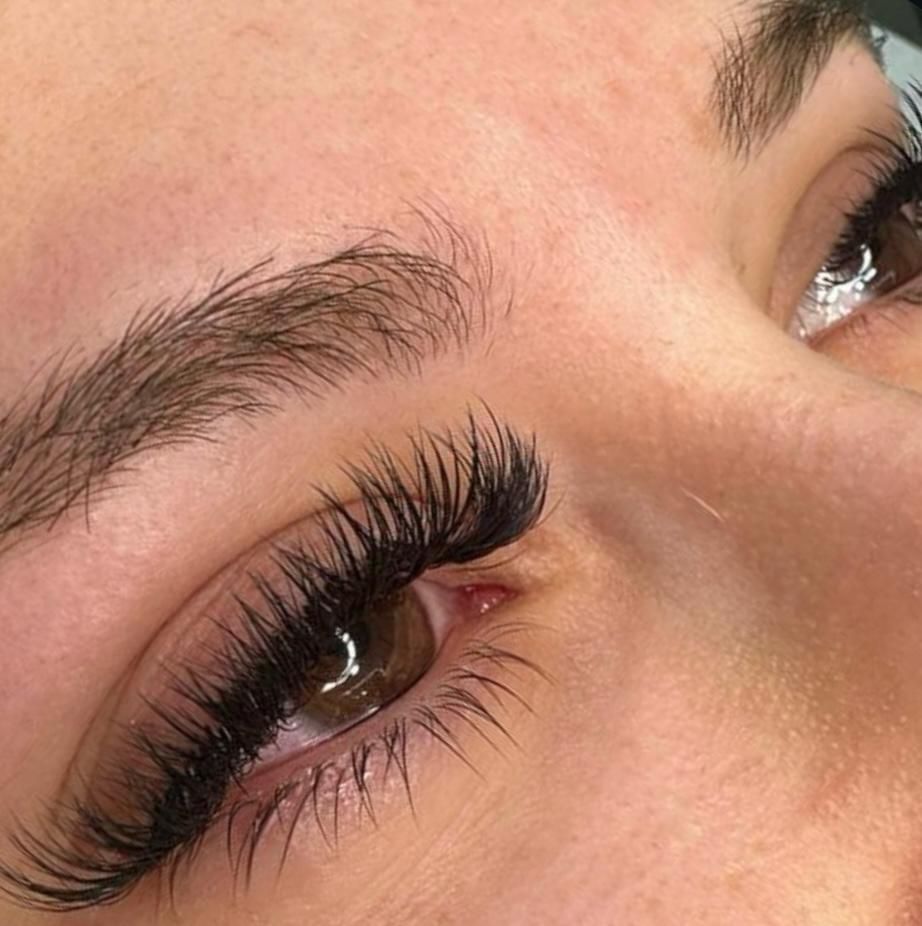 Primer plano del ojo de una persona con pestañas oscuras, gruesas y extendidas y cejas rellenas.