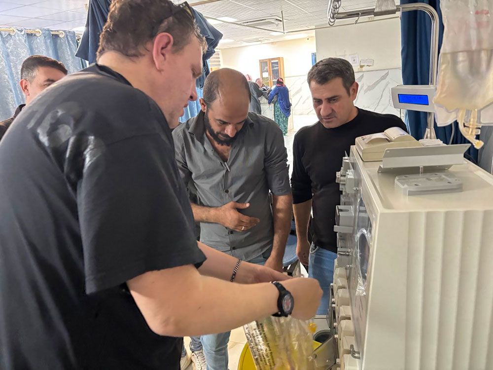 Drei Männer untersuchen medizinische Geräte in einer Gesundheitseinrichtung. Ein Mann in einem schwarzen Hemd justiert ein Gerät.