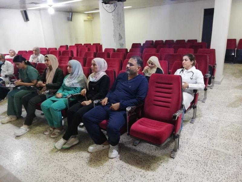 Menschen sitzen in einem kleinen Auditorium mit roten Stühlen, die in einem spärlich besetzten Raum nach vorne blicken.