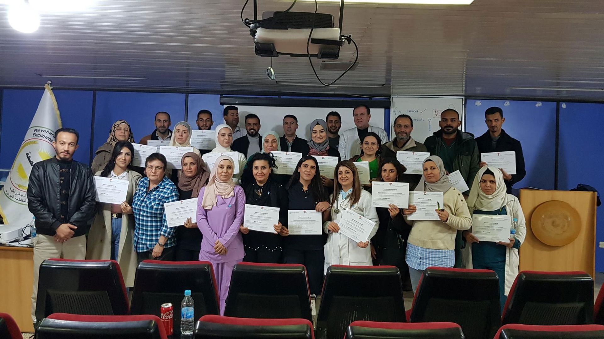 Group of people holding certificates, posing in an auditorium.