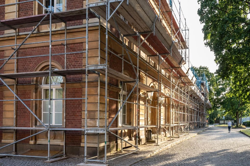 Backsteingebäude Ein Backsteingebäude, das an einer von Bäumen gesäumten Straße renoviert wird, ist von einem Gerüst umgeben.