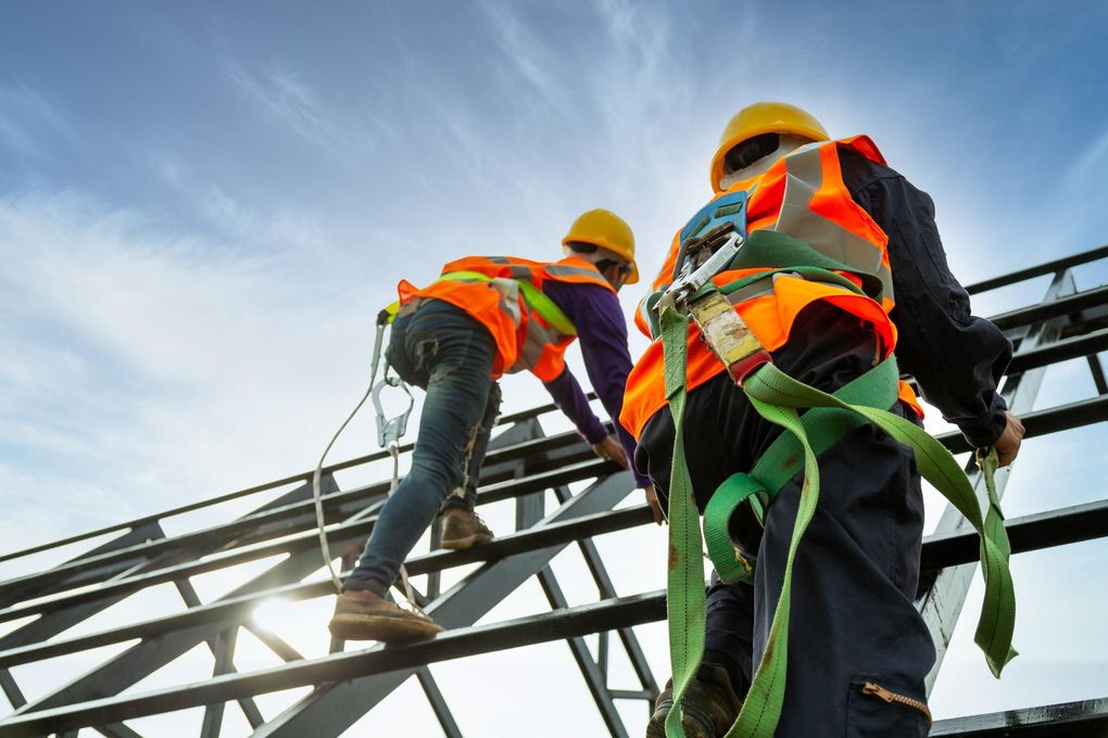 Bauarbeiter mit Schutzhelmen Bauarbeiter mit Schutzhelmen und orangefarbenen Westen steigen vor blauem Himmel ein Metallgerüst hinauf